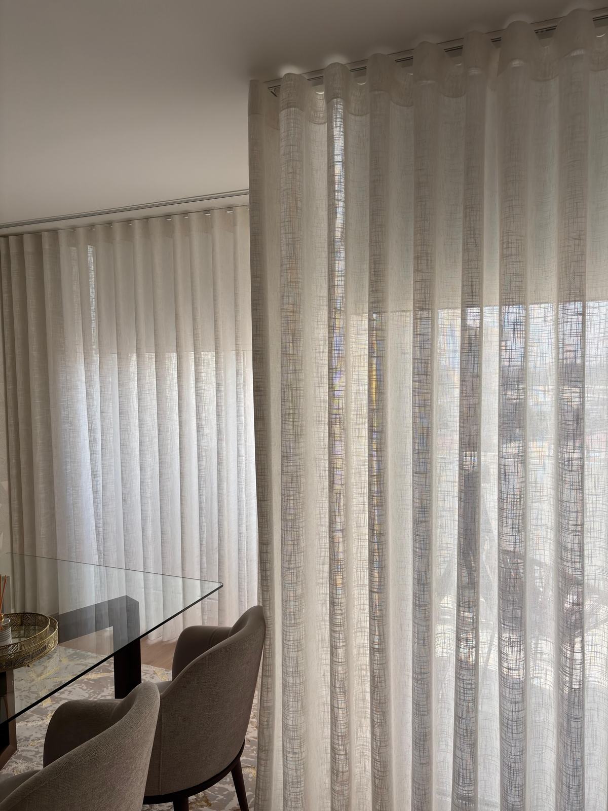 Cortinado de onda em linho junto a uma mesa de jantar de vidro
