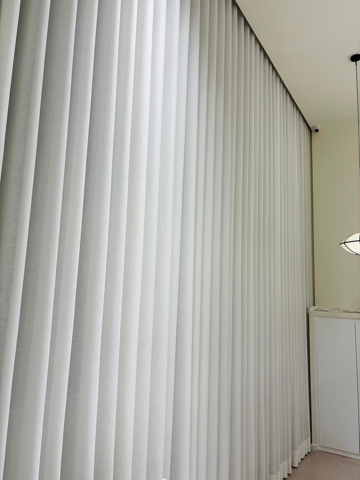 Pormenor das pregas de um cortinado de onda branco, do teto ao chão