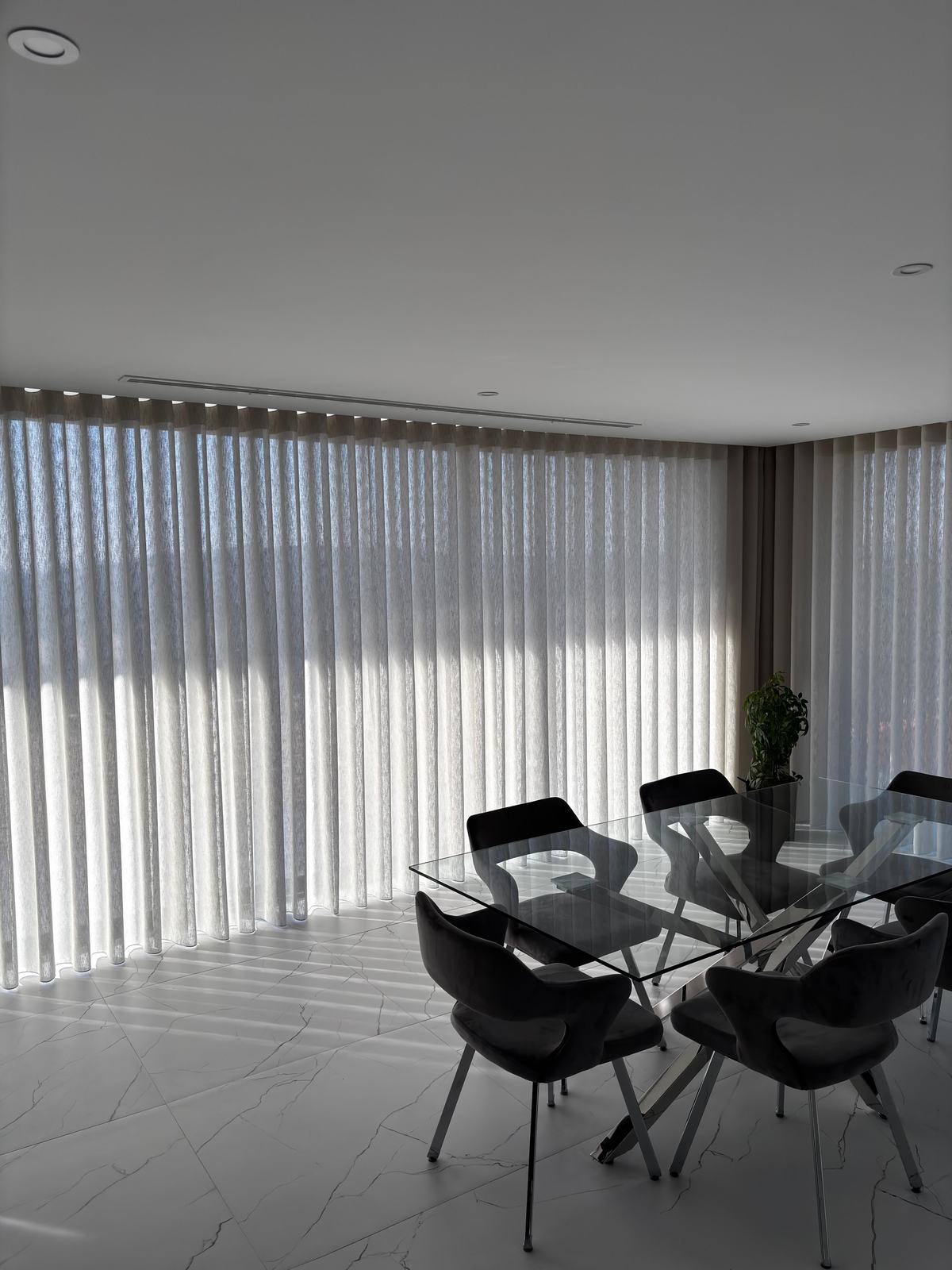 Sala de jantar com mesa de vidro e cadeiras pretas, com cortinados de onda translúcidos