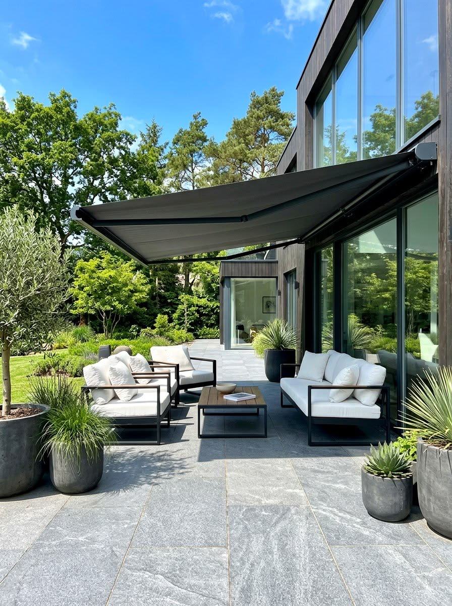 Toldo de braço articulado em tela antracite sobre um terraço envidraçado com vista para o jardim